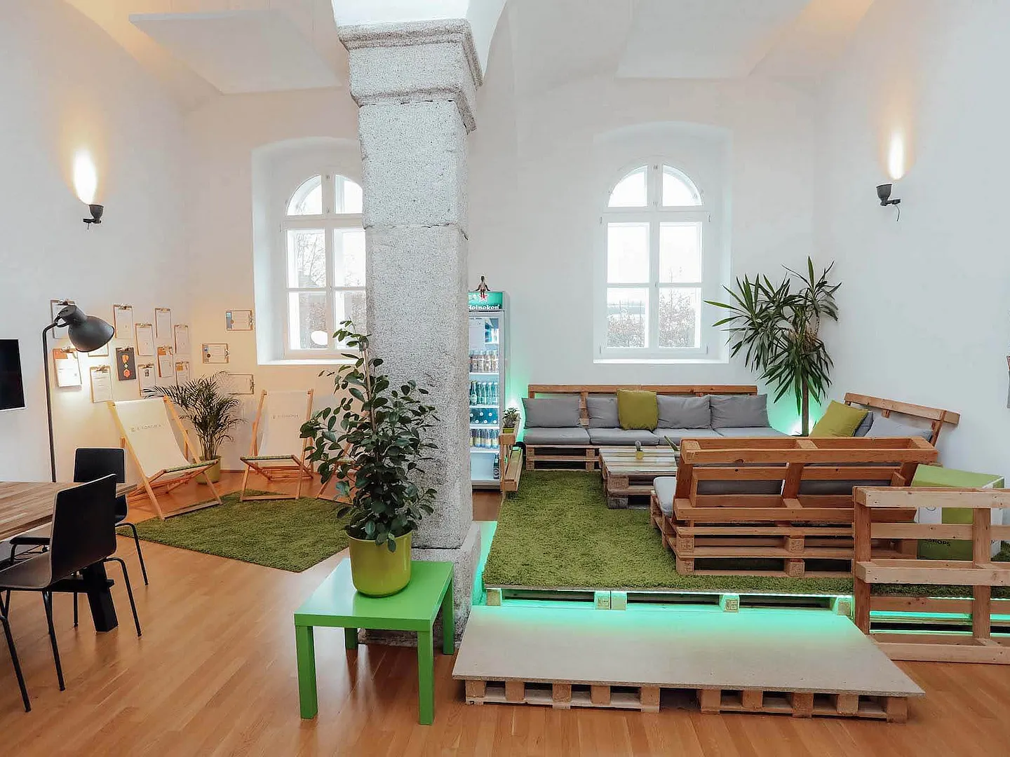 Büroraum in der Dragonerkaserne Wels mit Gewölbedecke, Steinsäule, Rundbogenfenstern und Lounge aus Holzpaletten